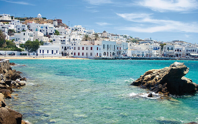 ein Bild eines Strandes auf Mykonos mit Blick auf weiße Gebäude und das Meer