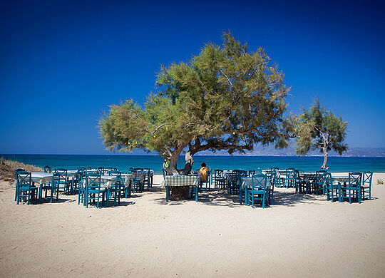 ein Bild eines Strandes auf Naxos mit Baum und blauen Tischen