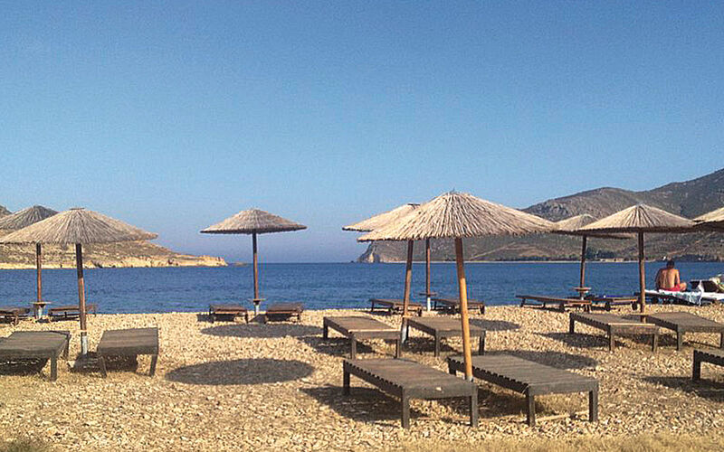 ein Bild eines Strandes auf Patmos mit Blick auf Sonneschirme, Liegestühle, den Strand und das Meer