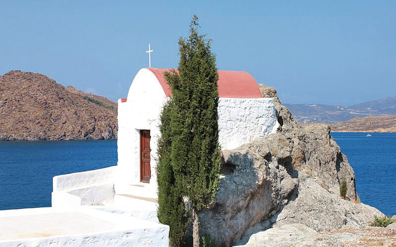 ein Bild von Patmos mit Blick auf ein kleines Gebäude, einen Baum und das Meer im Hintergrund