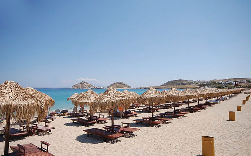 ein Bild eines Strandes auf Mykonos mit Blick auf Sand, Sonnenschirme und Liegestühle