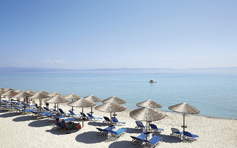 ein Bild eines Strandes auf Chalkidiki, der zu dem Hotel Ammon Zeus gehört, mit Sonnenschirmen, Liegestühlen und Blick auf das Meer