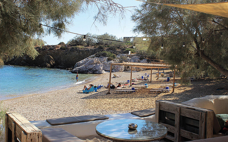 ein Bild des Apantima Strandes auf Antiparos mit Liegestühlen, Sonnenschirmen und Bäumen